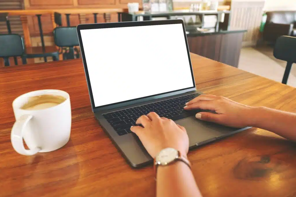 A woman using and typing on laptop with blank white screen